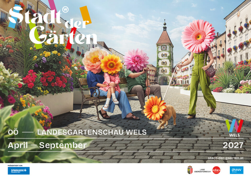 Werbesujet der Landesgartenschau Wels 2027 in Oberösterreich mit blühender Innenstadt, Stadtplatz, zahlreichen Blumenarrangements und dem historischen Ledererturm im Zentrum von Wels.